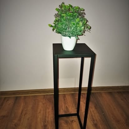 Zielona roślina w białej ceramicznej doniczce na wysokim czarnym metalowym stojaku